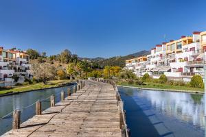 un pont en bois sur une rivière à côté des bâtiments dans l'établissement RentitSpain Charming Apartment in Parque Botanico Resort & Country Club, Marbella, Estepona, Benahavis, à Estepona