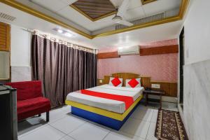 a bedroom with a bed and a red chair at OYO Flagship Hotel Ravi Palace in Rajkot