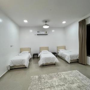 três camas num quarto com paredes brancas e um tapete em استراحة روضة الوادي em Nizwa