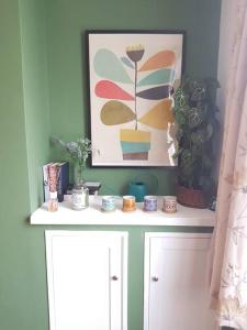 a white shelf with plants and a painting on a wall at The Cosy Home in Burton. Sleeps 5. Fast Wi-fi in Burton upon Trent