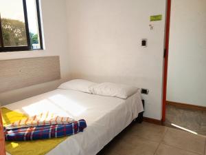 a small bedroom with a white bed with a window at Tesoro Andino in La Tebaida