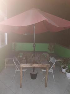 une table en bois avec un parasol et des chaises roses dans l'établissement chez albino guest house, à São Filipe