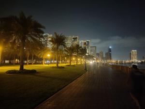 a park with palm trees and a city at night at Arnim Suite - 3 Bedrooms Apartment in Sharjah