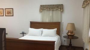 a bedroom with a bed with white sheets and a lamp at Center Suiço Flats in Campos do Jordão