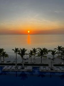 a sunset over the ocean with palm trees and a pool at Ocean Reef Island Apartment in Panama City
