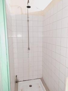 uma casa de banho em azulejos brancos com um chuveiro e um WC. em Auberge Mariama BA em Gorée