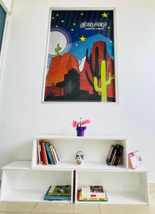 a white shelf with books and a painting on the wall at Hospedaje Casa Cultural Saberes in Neiva