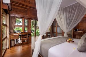 a bedroom with a white bed with a desk and a desk at Berlima Wooden Lodge by Pramana Villas in Ubud