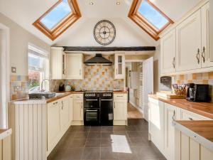 a kitchen with white cabinets and a clock on the wall at Curlew Cottage in Caister-on-Sea