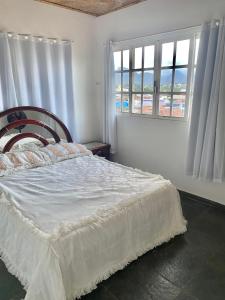 um quarto com uma cama com lençóis brancos e janelas em CASA EM GUARAPARI em Guarapari
