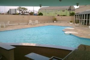 a large swimming pool with chairs and a building at Flat 1 qto, piscina, loc central in São José dos Pinhais +6 photos