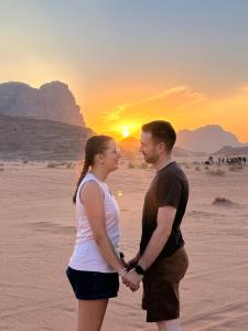 a man and a woman standing on the beach watching the sunset at MAGIC RUM lUXURY HUSSEN in Wadi Rum
