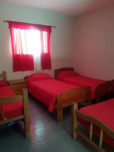 1 dormitorio con 3 camas y una ventana con sábanas rojas en Departamentos PEUQUE en Comodoro Rivadavia