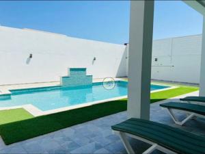 basen z dwoma zielonymi ławkami w budynku w obiekcie villa jassem w mieście Awlād ‘Umar