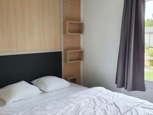 a bed with two pillows on it next to a window at Chalet Confort 2 Chambres avec Piscine Chauffée et Climatisation en Bretagne Sud - FR-1-783-19 in Marzan +25 photos
