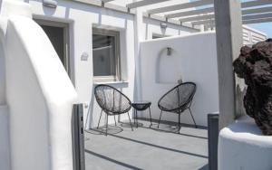 2 chaises assises sur une terrasse avec un bâtiment dans l'établissement AK Suites, à Imerovigli