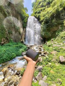 uma pessoa segurando uma câmera em frente a uma cachoeira em Ashapuri Cottage near Rupi Raila Waterfall em Sainj