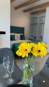 a vase with yellow flowers on a table with two wine glasses at Apart-hotel Happy Life in Alicante