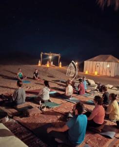 a group of people sitting on the beach at night at Horaz Merzouga Camp in Merzouga