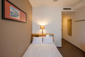 Schlafzimmer mit einem Bett mit weißer Bettwäsche in der Unterkunft Hotel JIN Morioka Ekimae in Morioka