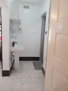 Baño blanco con lavabo y puerta en Cacecy Luxury Homes 2 -Bedroom, en Bungoma