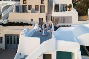 a woman sitting at a table in the courtyard of a white building at Heavens Edge in Imerovigli