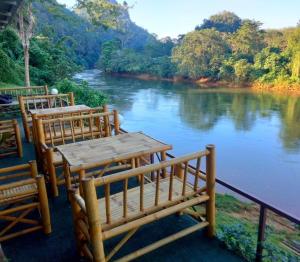 two wooden tables and chairs next to a river at Khlongsaeng farmstay in Ban Ta Khun