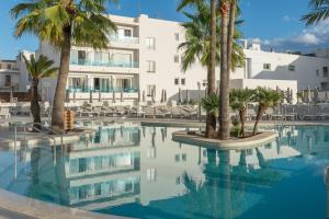 a swimming pool with palm trees in front of a building at Hotel Cala Bona in Cala Bona