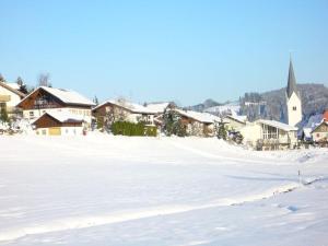 pokryte śniegiem pole z domami i kościołem w obiekcie Haus Nett Modern retreat w mieście Stiefenhofen
