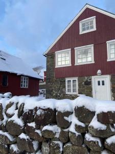 uma cerca de pedra em frente a uma casa vermelha com neve em Seaside Cottage em Oyndarfjørður