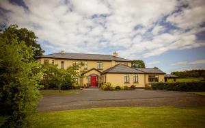 une maison jaune avec une porte rouge dans une allée. dans l'établissement Cahergal Farmhouse B&B, à Newmarket on Fergus