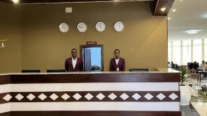 dos hombres parados detrás de un mostrador en un vestíbulo con relojes en la pared en Haile Hotel Wolaita, en Sodo