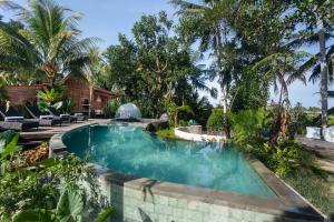 einen Pool im Hinterhof mit Palmen in der Unterkunft Berlima Wooden Lodge by Pramana Villas in Ubud
