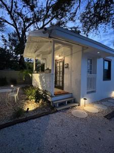 a small white house with a porch and a chair at Cracker Cow Cottages - Cottage B in Fort Myers