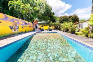 a swimming pool next to a yellow wall with a painting on it at Maison d'invités dans jardin tropical avec piscine à Tahiti in Atiue