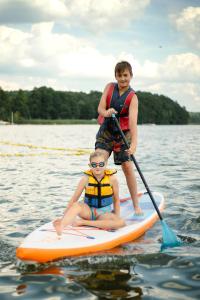 two boys on a paddle board in the water at RiW Małe Swory - Domek pływający Houseboat in Małe Swornegacie