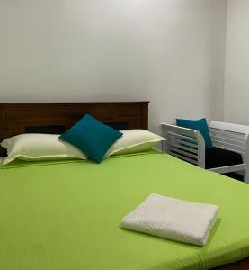 ein grünes Bett mit blauen und weißen Kissen und einem Stuhl in der Unterkunft Cinnamon apartment in Panadura