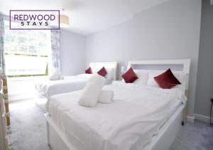 two white beds with red pillows in a bedroom at Spacious Serviced Apartment for Contractors and Families, FREE WiFi & Netflix by REDWOOD STAYS in Farnborough