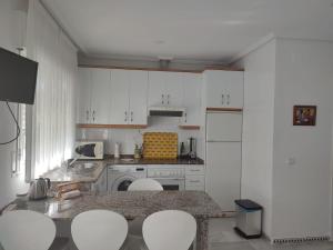 a kitchen with white cabinets and a table and chairs at Apartamento Pinar del Atlántico La Barrosa in Chiclana de la Frontera