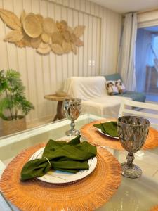 a table with two plates and wine glasses on it at Apartamentos no Condomínio Beach Village Fortaleza - Praia do Futuro - Por CasAmarInn in Fortaleza