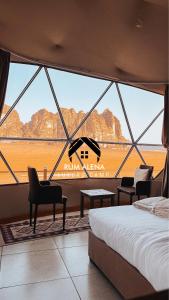 una camera da letto con una grande finestra con un letto e sedie di RUM ALIENA LUXURY CAMP a Wadi Rum
