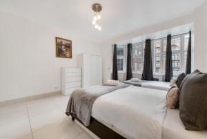 a white bedroom with two beds and windows at 2Bd Flat Opp Harrods - Sleeps 5 in London