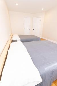 two beds in a bedroom with white walls and wood floors at Elegant & Spacious 3-Bed Space near NYC in Jersey City