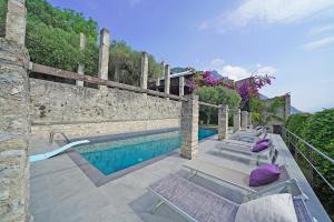 een zwembad met ligstoelen naast een stenen muur bij Villa Rachele: stunning luxury villa in centre Gargnano with private pool and breathtaking views in Gargnano