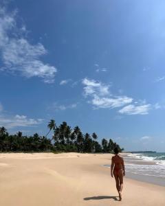 Una mujer caminando por la playa con una tabla de surf en Neem Tree Ambalangoda, en Ambalangoda