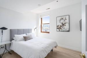 a white bedroom with a bed and a window at Le Nomade MTL in Montréal