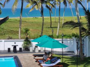 two people sitting on lounge chairs under an umbrella by a pool at Darshana Beach Hotel in Kosgoda