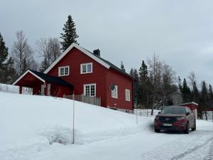 une voiture garée devant une maison rouge dans la neige dans l'établissement Kleiva 8 Skorovas, à Namsskogan
