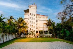 a large white building with palm trees in front of it at KAMAT'S DAFFODIL RESORT GOA in Pilerne