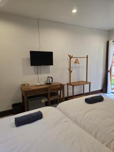 two beds in a room with a tv and a desk at The Old City Rooms in Chiang Mai